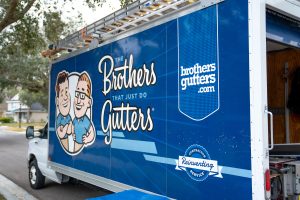 Image of a The Brothers That Just do Gutters truck. The blue truck has the logo an text for the main website brothersgutters.com