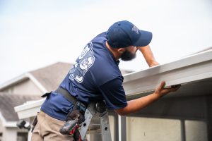 Gutter installer works to install a white gutter on a house