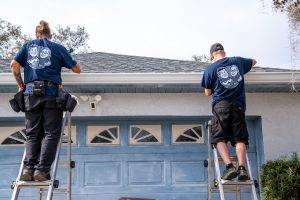 Two gutter installers install a white gutter on to a house.