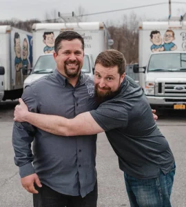 Two The Brothers That Just Do Gutters Employees embrace in front of The Brothers That Just Do Gutters trucks